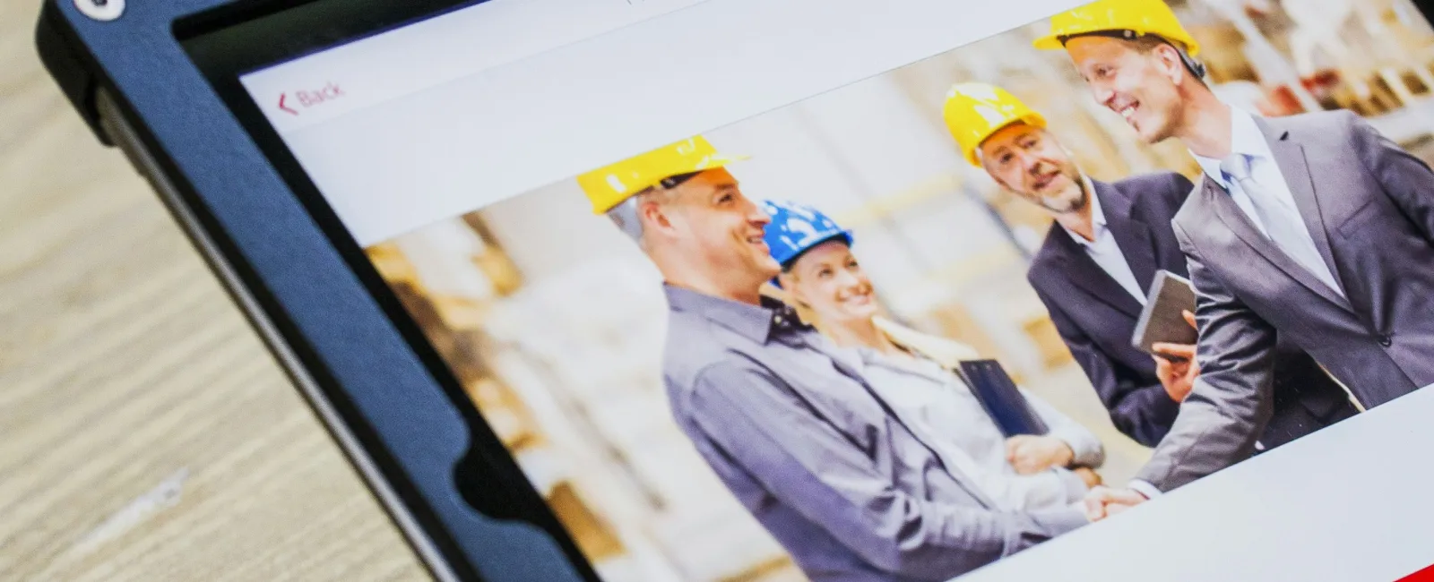 Tablet screen displays a group of workers in safety helmets shaking hands in a warehouse setting.