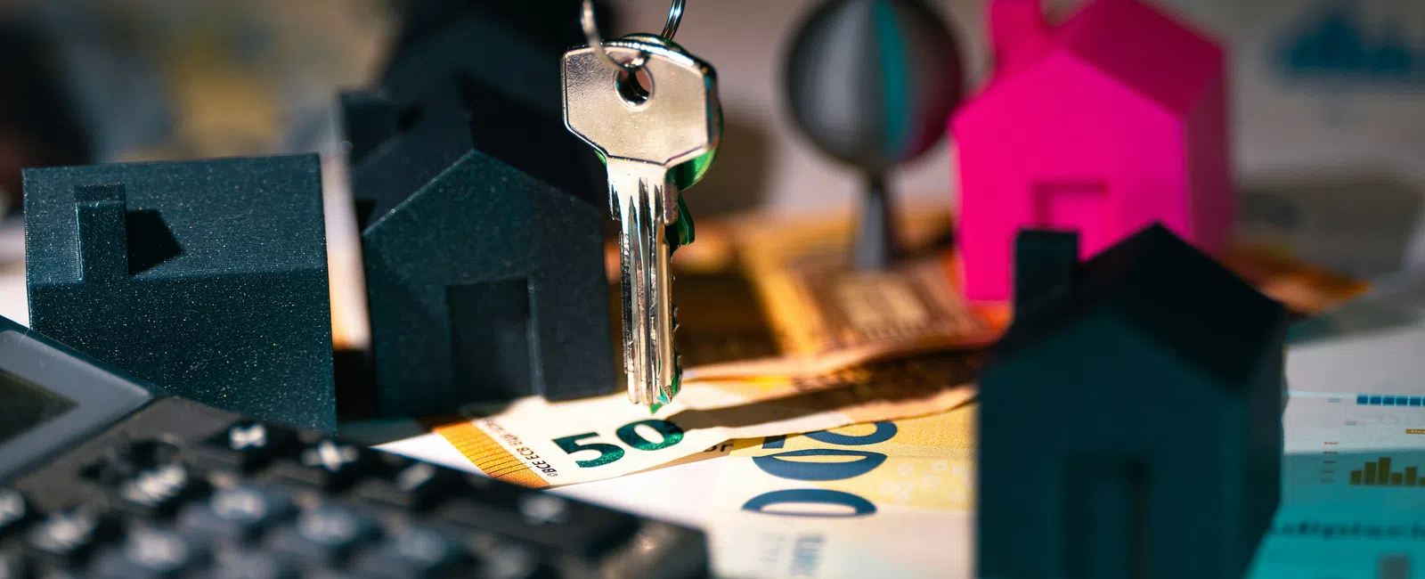 House key hanging above miniature house models, calculator, and Euro banknotes symbolizing real estate investment.