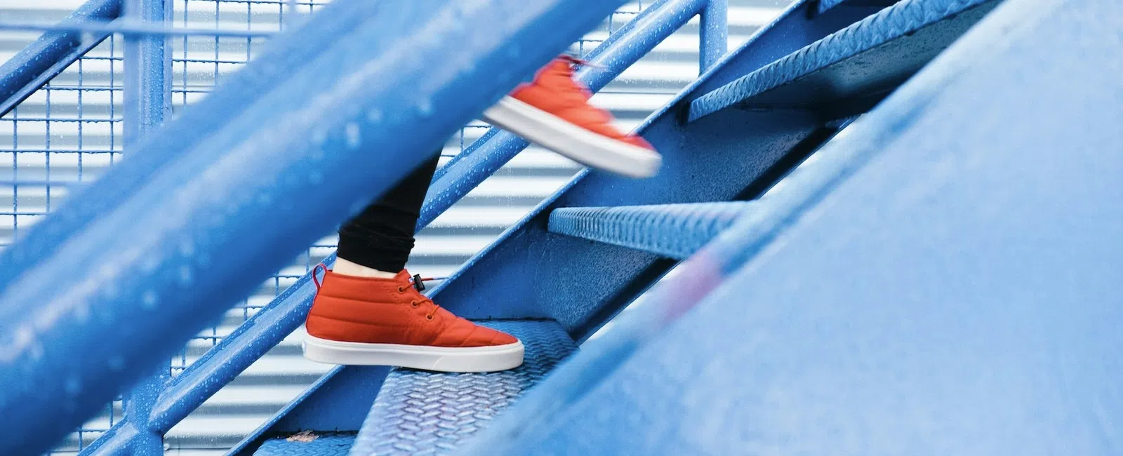 Person wearing bright orange sneakers walking up blue metal stairs with railing in an urban setting