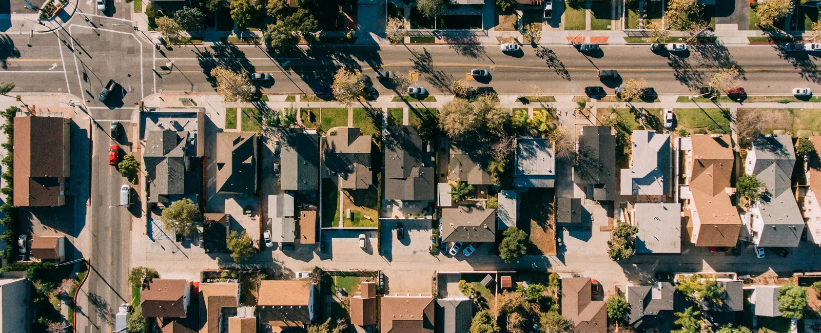 Aerial view of a suburban neighborhood with rows of houses, streets, cars, and greenery on a sunny day.