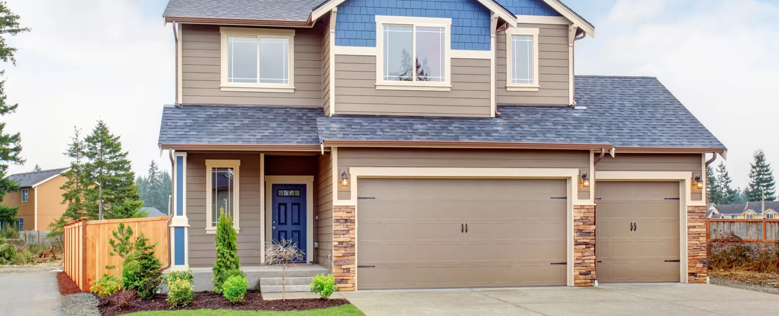 Modern two-story house with blue and beige siding, three-car garage, and landscaped front yard under blue sky.