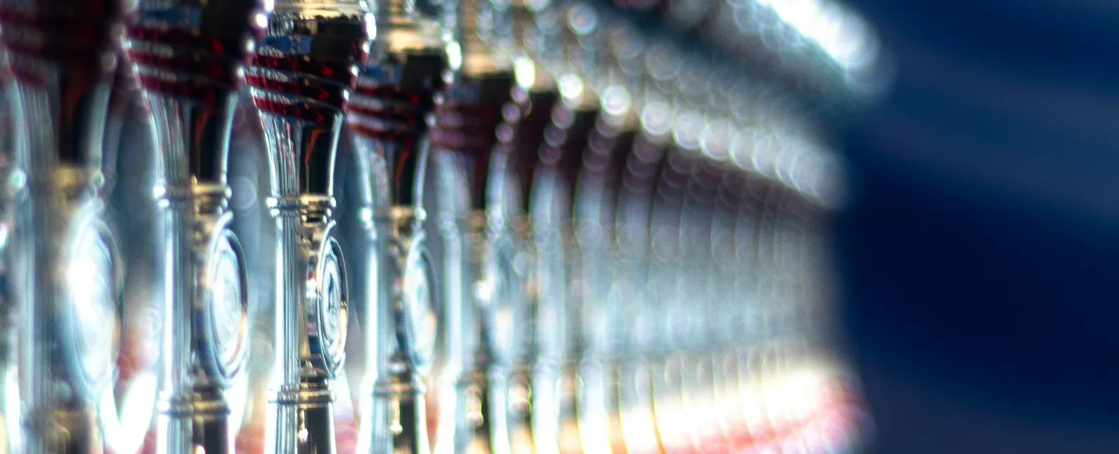 Row of shiny silver trophies with red accents displayed on a blue cloth-covered table in soft focus.