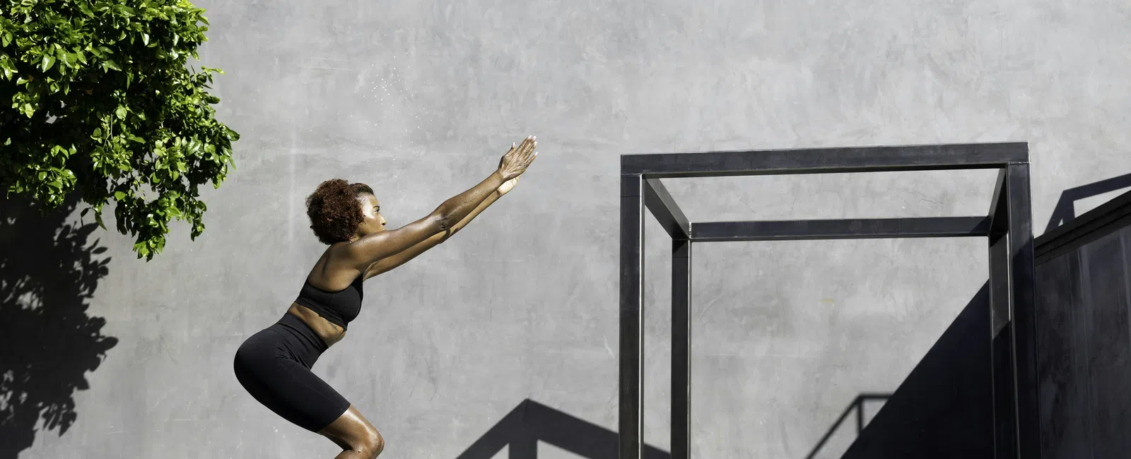 Woman in athletic wear performing a squat exercise outdoors against a gray wall with gym bag nearby.