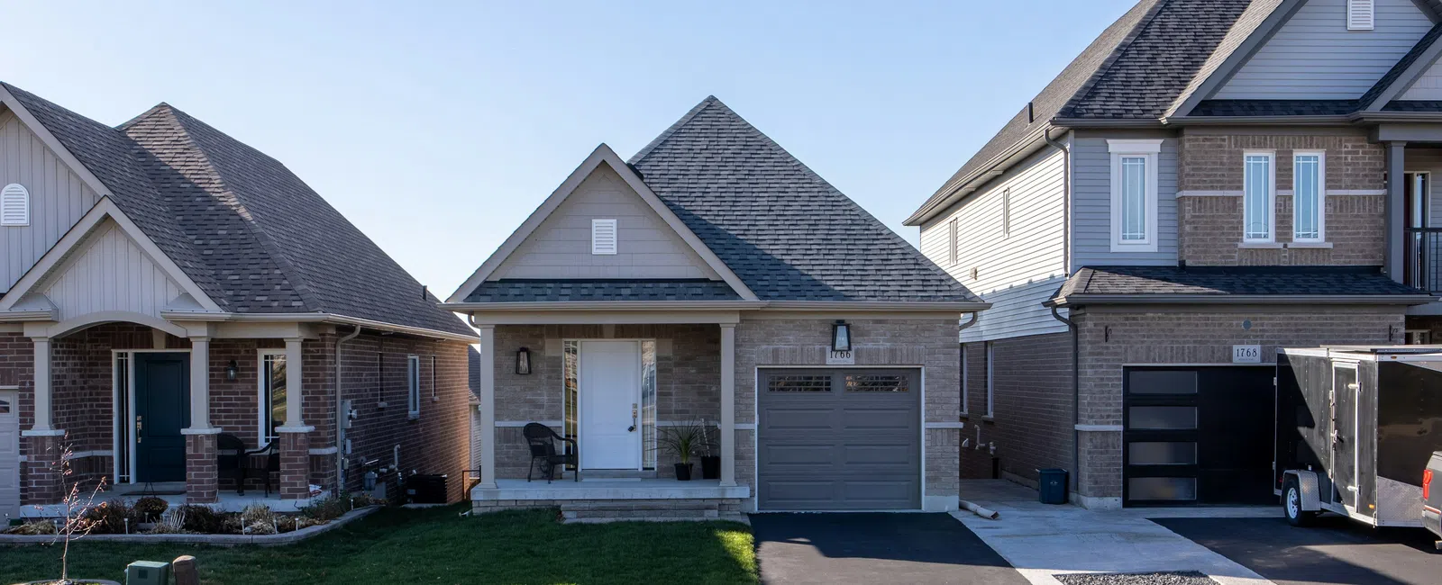 Suburban street with three modern single-family homes featuring garages, lawns, and driveways under a clear blue sky.