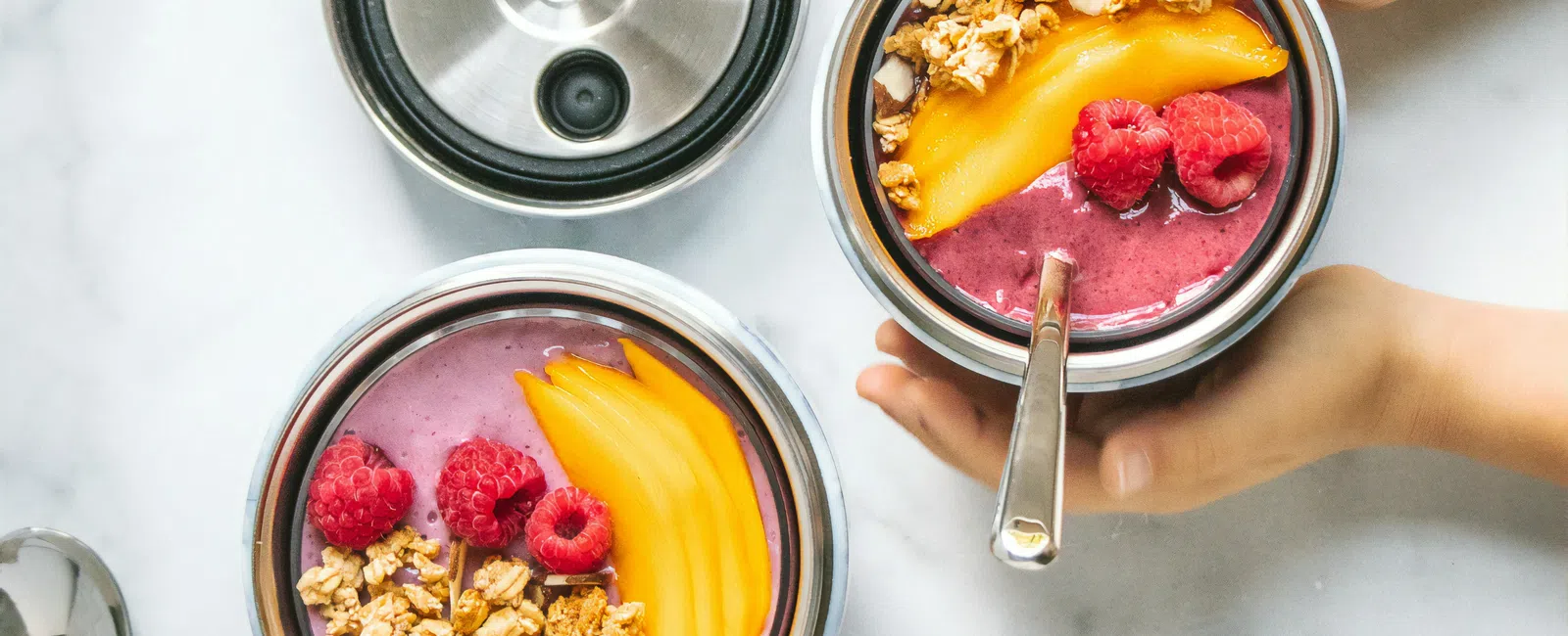 Top view of smoothie bowls with mango, raspberries, granola, and blackberries on a white marble surface