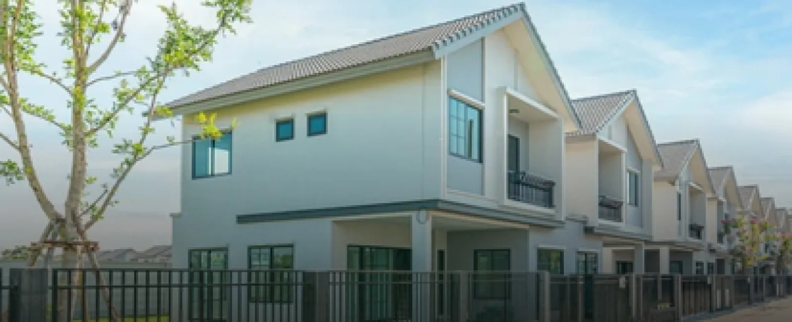 Row of modern two-story white houses with gray roofs and black fences under a clear blue sky.