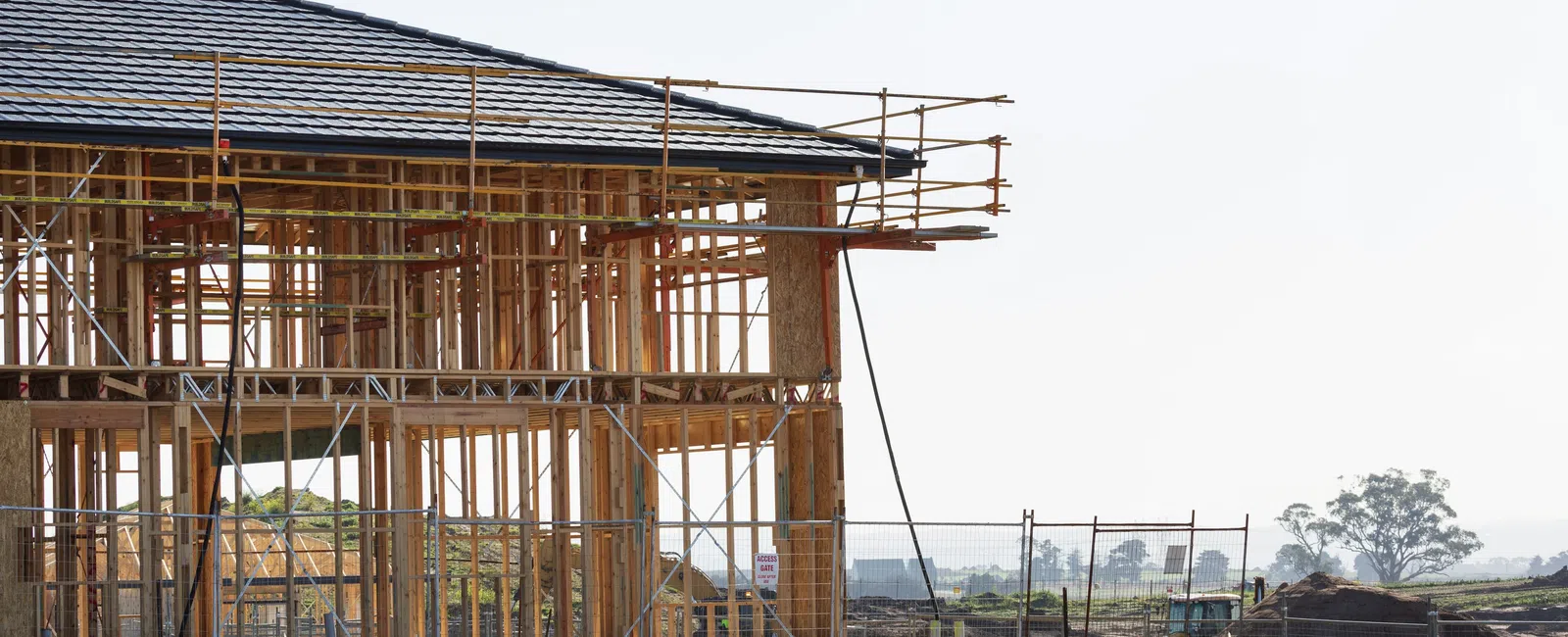 Wooden frame of a house under construction with scaffolding on a clear day in an open area.