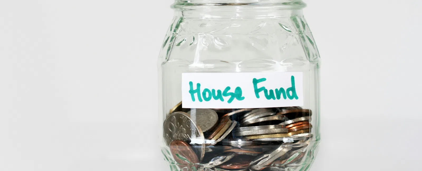 Glass jar labeled House Fund filled halfway with assorted coins for savings or budgeting.