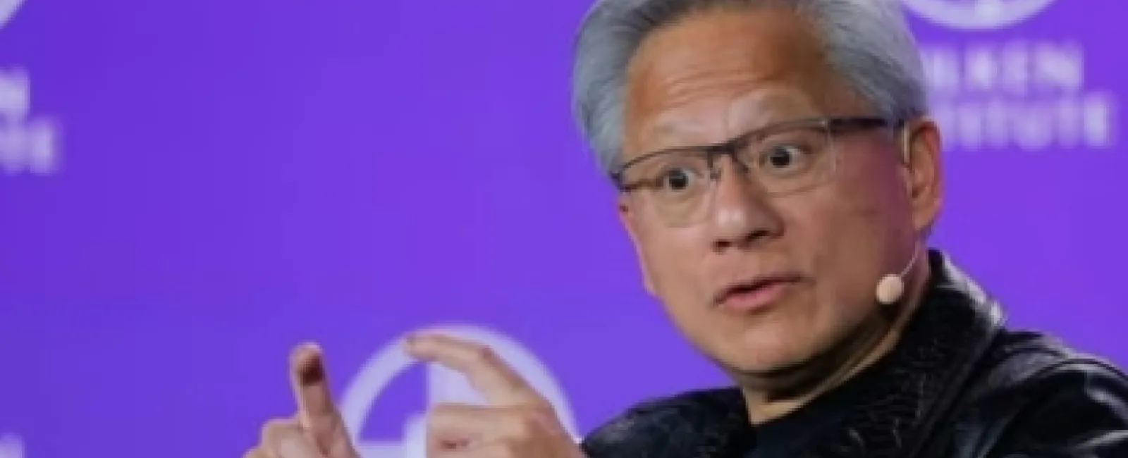 Man with gray hair and glasses speaking with hand gestures wearing black leather jacket and microphone headset on purple background