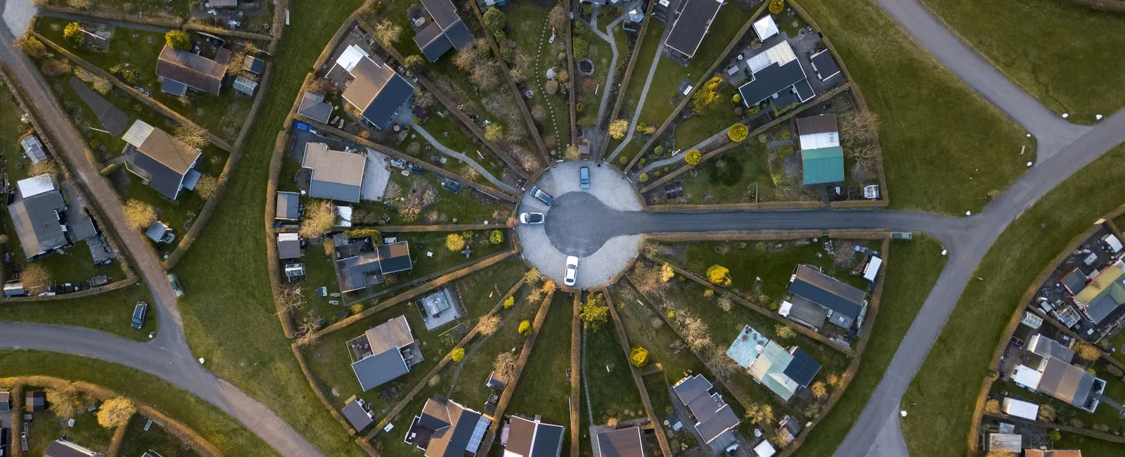 Aerial view of a circular residential neighborhood with houses arranged around a central roundabout and green spaces.