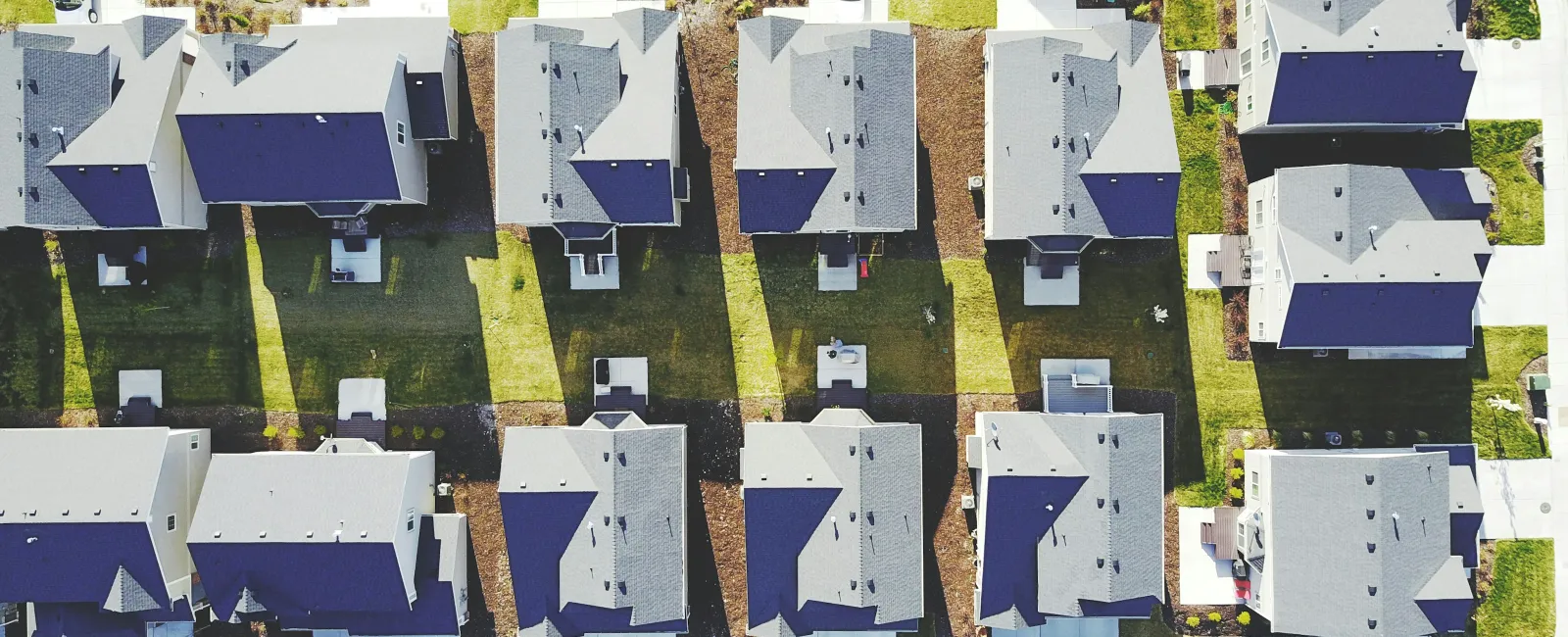 Aerial view of a suburban neighborhood with rows of houses casting long shadows on lawns and streets.
