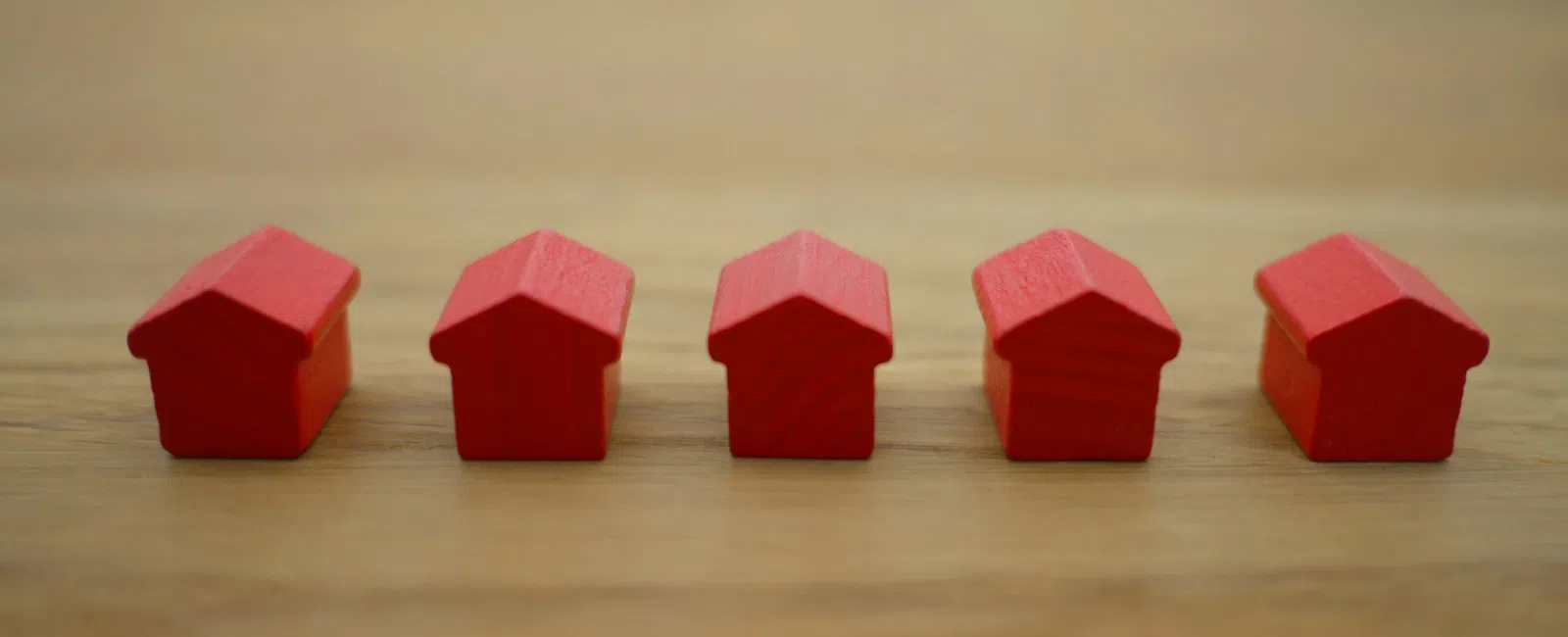 Five small red wooden house models lined up on a wooden surface with blurred background.