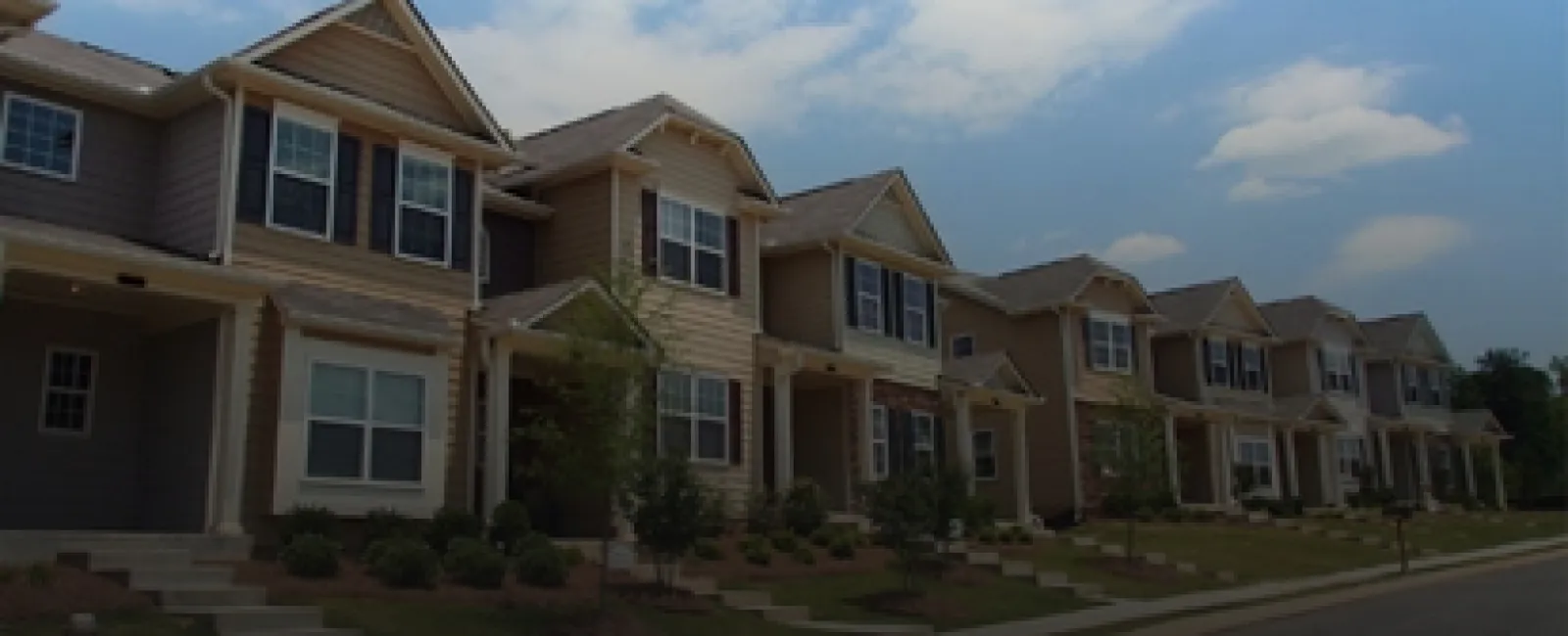 Row of modern two-story townhouses with beige siding and manicured front lawns under blue sky.