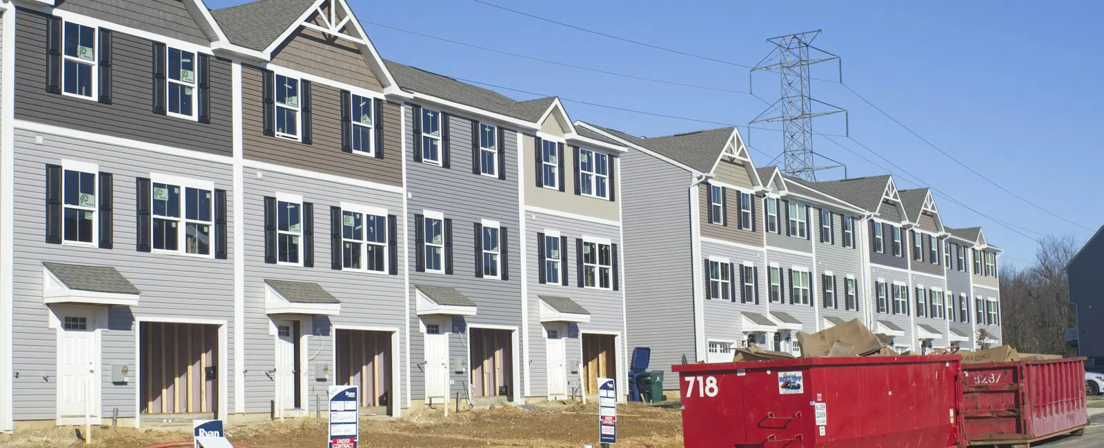 Newly constructed multi-story townhouses under clear blue sky with construction dumpsters in front.