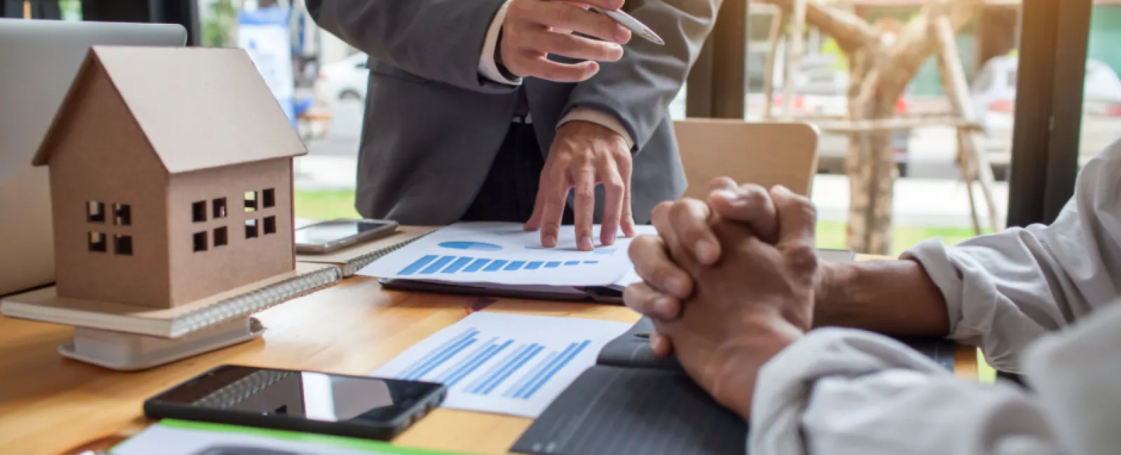 Real estate agent discussing housing market charts with client at office desk with house model and calculator.