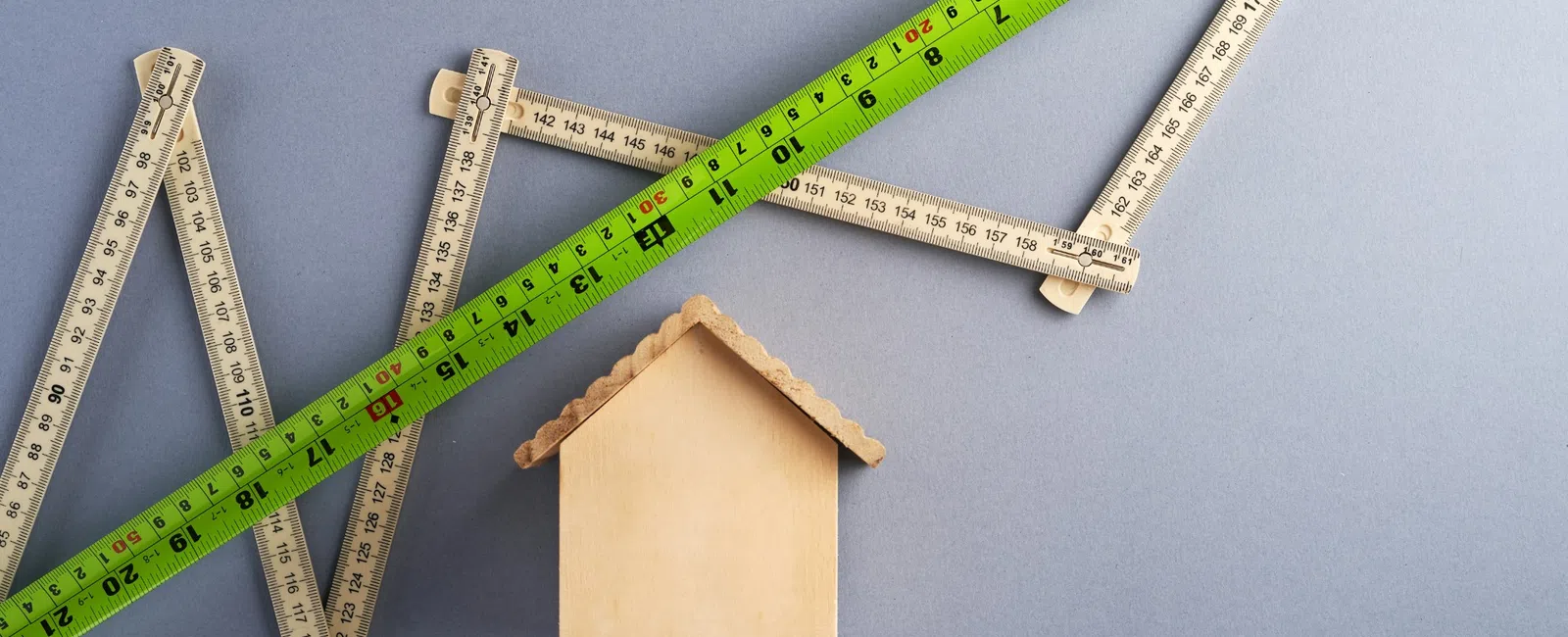 Wooden house model with folding rulers forming an upward arrow, symbolizing growth in real estate or construction.