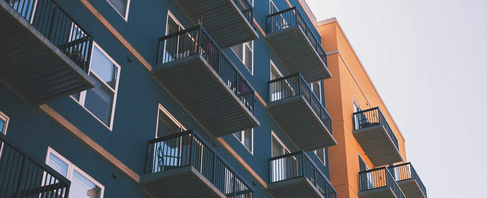 Modern apartment building with blue and orange facades featuring multiple balconies under clear sky.