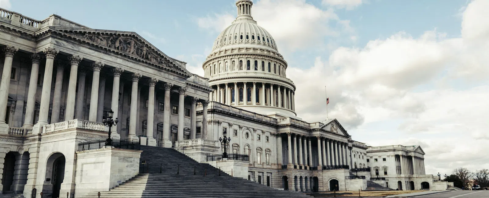 The United States Capitol building with its large dome and classical columns under a partly cloudy sky.