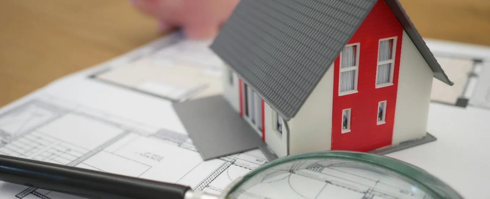 Miniature house model on architectural blueprints with magnifying glass and piggy bank in background