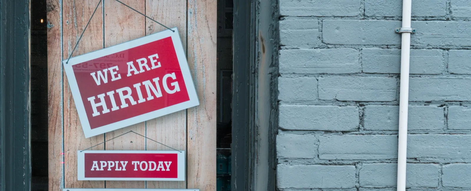 Red and white hiring signs on wooden background promoting job applications and recruitment.