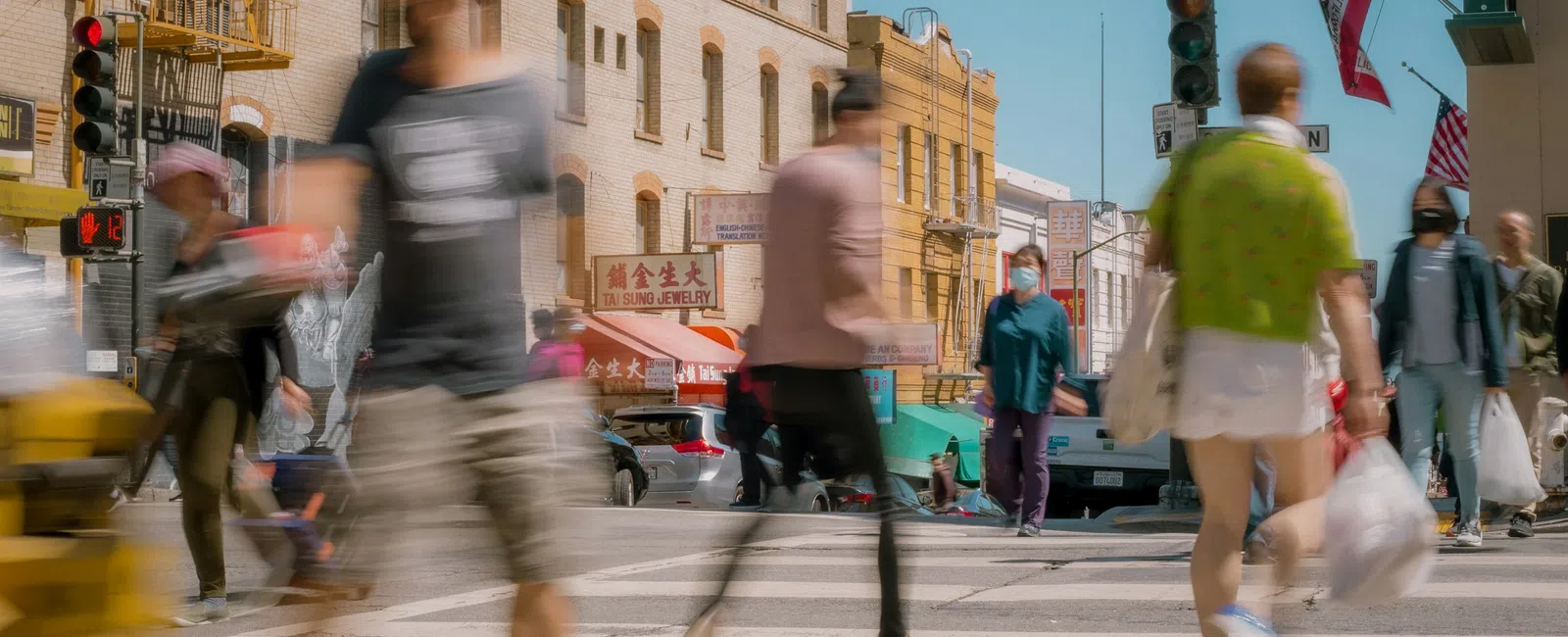 Blurred pedestrians crossing a busy street at Stockton with urban buildings and traffic lights in the background