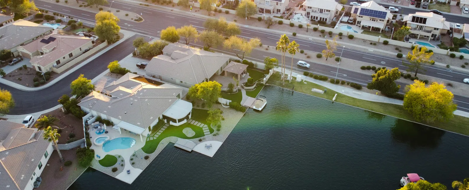 Aerial view of suburban homes with pools and waterfront along a calm lake at sunset.