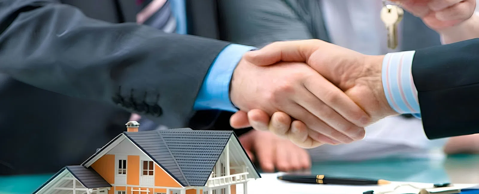 Close-up of handshake in business suits with a house model and person holding a key in background