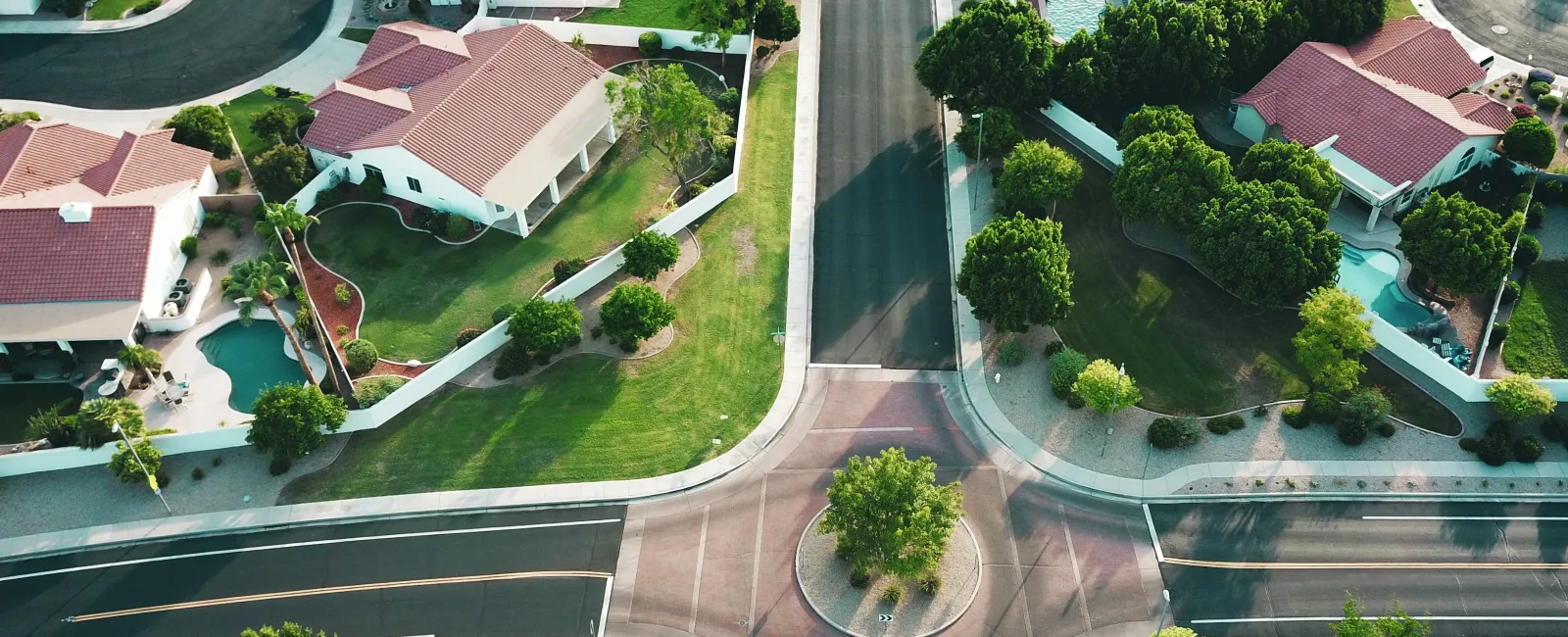Aerial view of suburban neighborhood with single-family homes, green lawns, trees, and a small traffic roundabout.