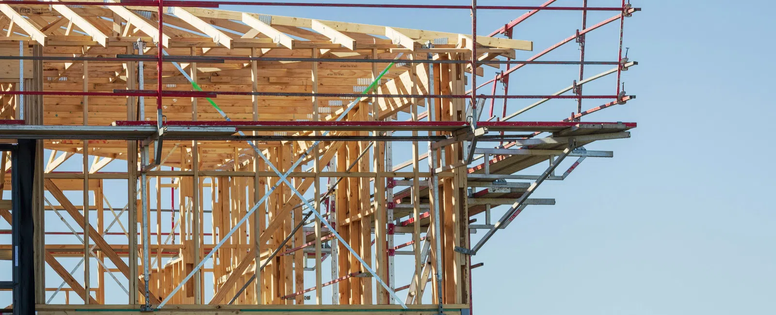 Wooden house frame under construction with scaffolding against clear blue sky.