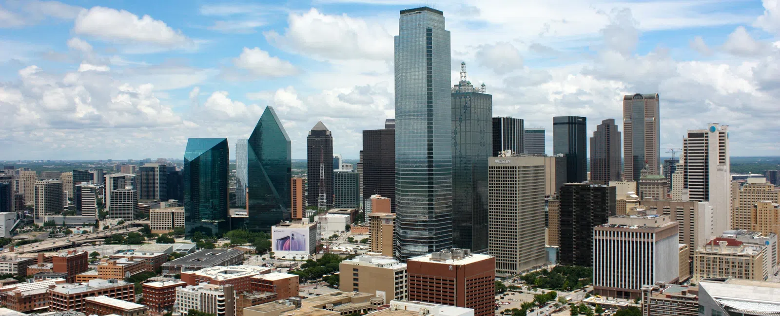 Downtown Dallas city skyline with tall skyscrapers under a partly cloudy blue sky.
