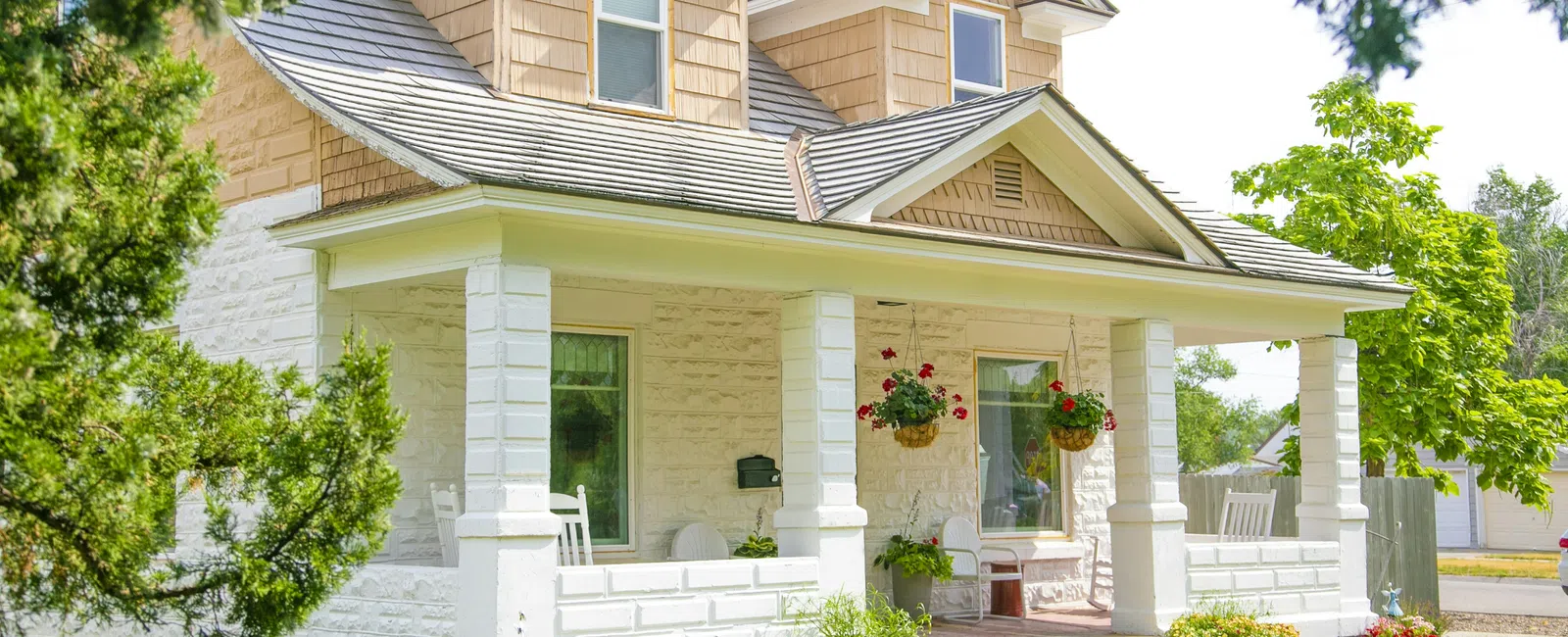 Bright sunny day view of charming white brick house with front porch, hanging flower baskets, and green lawn.
