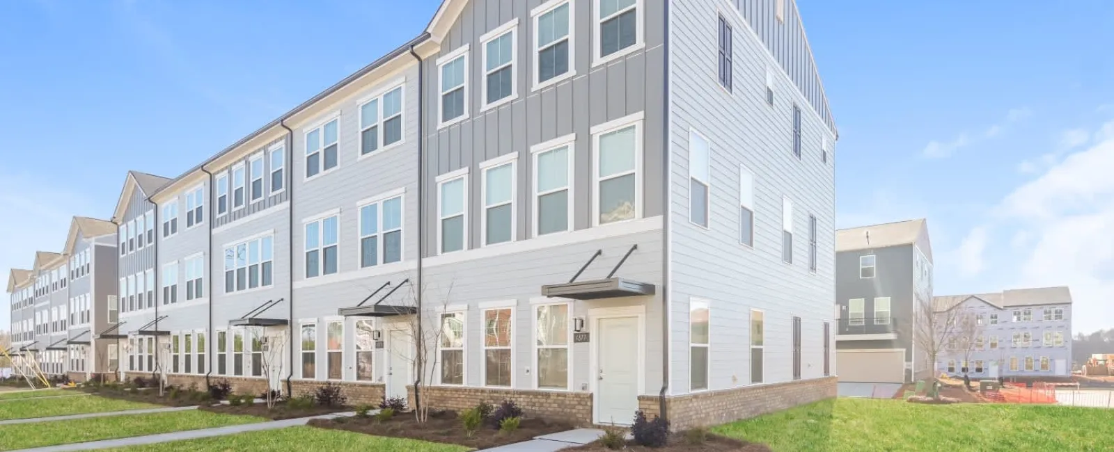 Modern three-story townhomes with gray siding and green lawns under a clear blue sky.