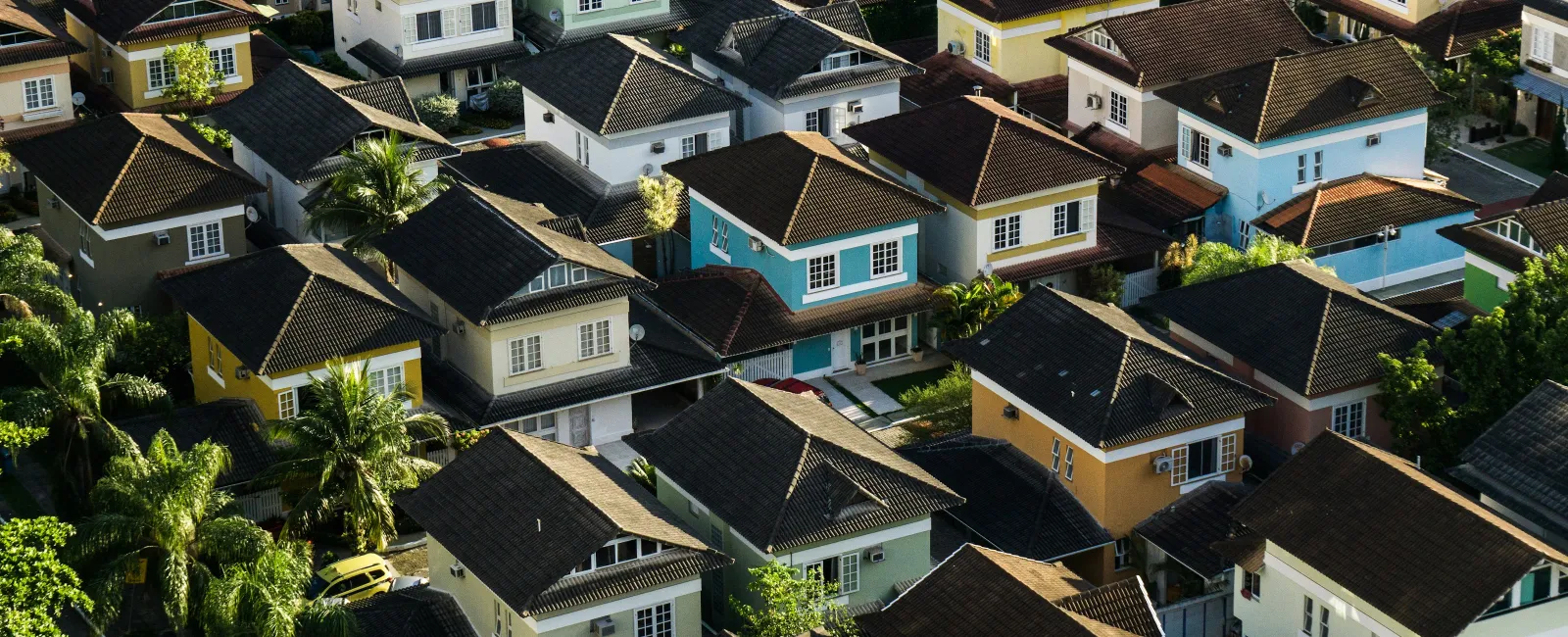 Aerial view of a suburban neighborhood with densely packed two-story houses and greenery under sunlight.