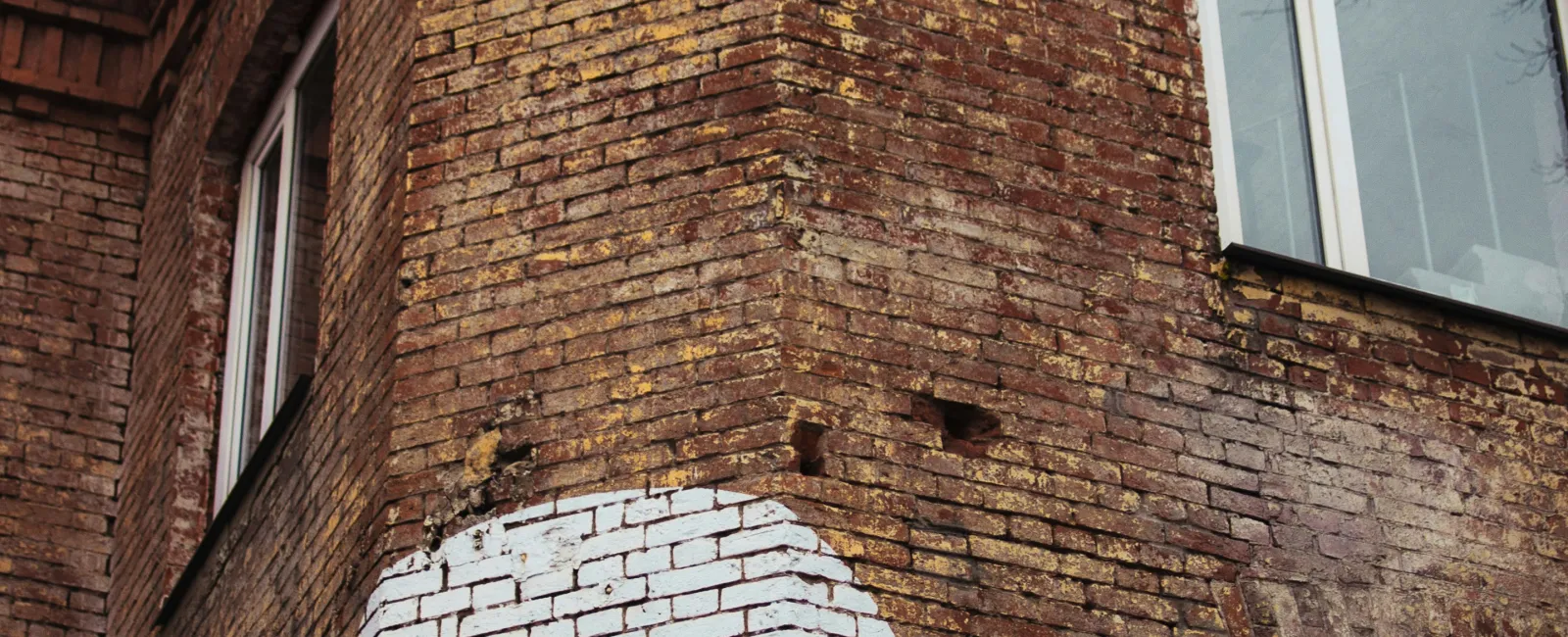 White number 9 painted on corner of aged red brick building with three windows and decorative brickwork.