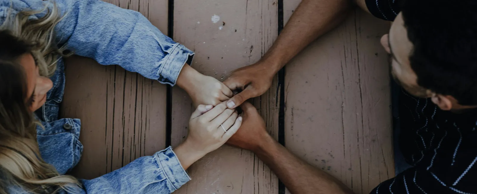 Couple holding hands across wooden table showing affection and connection, viewed from above