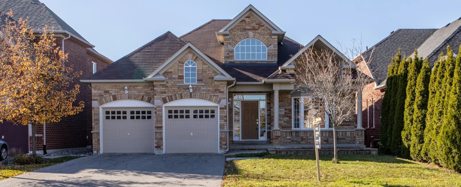 Two-story brick house with double garage, arched windows, and a manicured front lawn in a suburban neighborhood