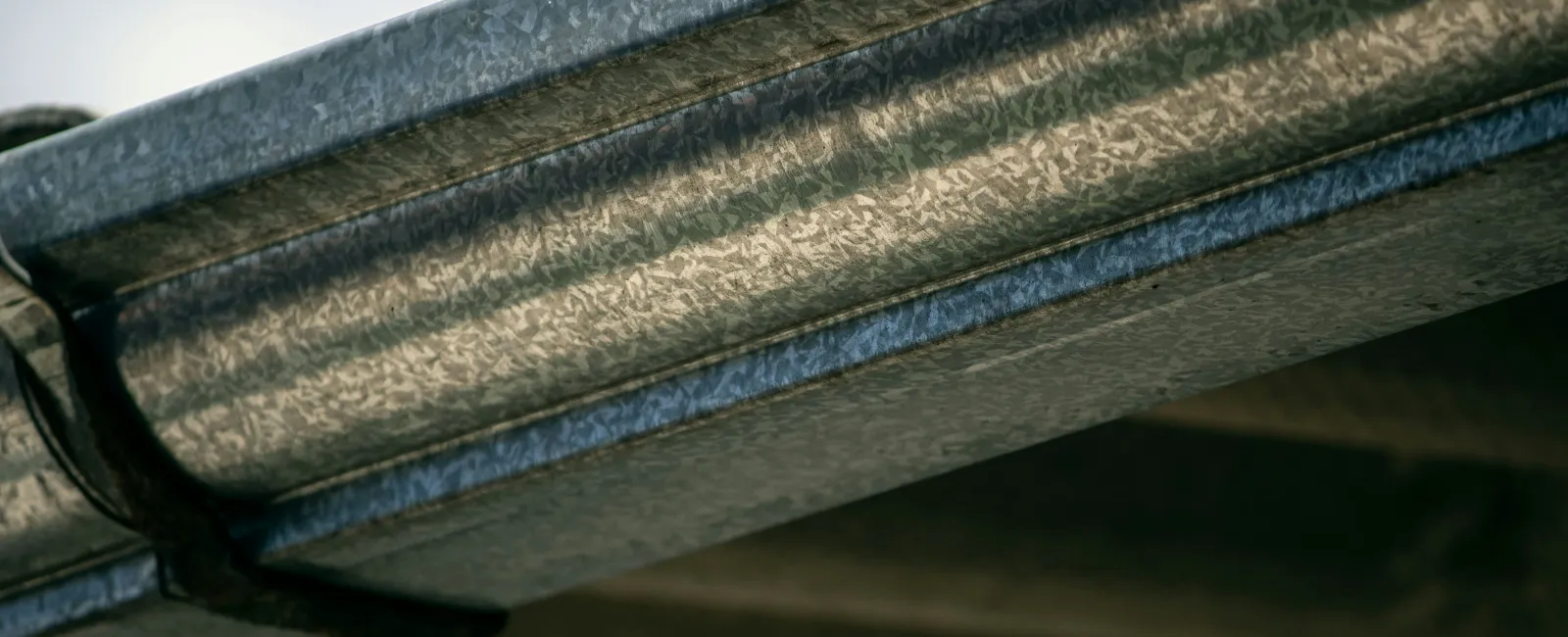 Close-up of galvanized steel gutter attached to roof edge with clear sky background