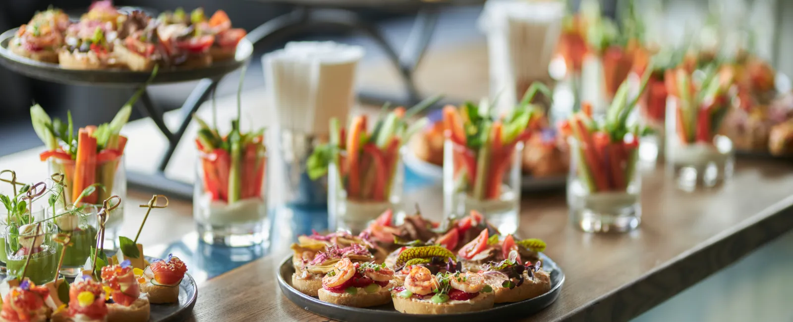 Assorted colorful appetizers and vegetable cups arranged on a wooden table for a catered event or party.