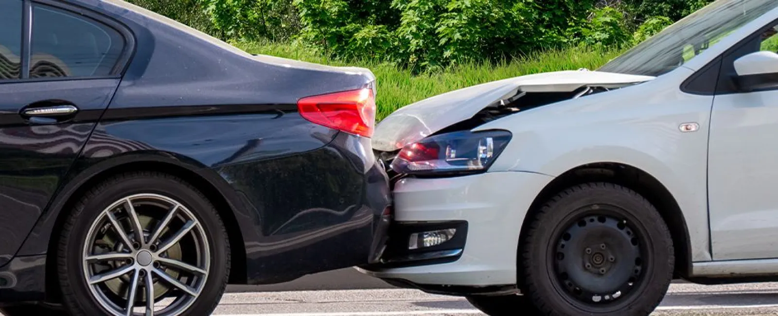 Rear-end collision between a white car and a black car on a sunny day with trees in the background.
