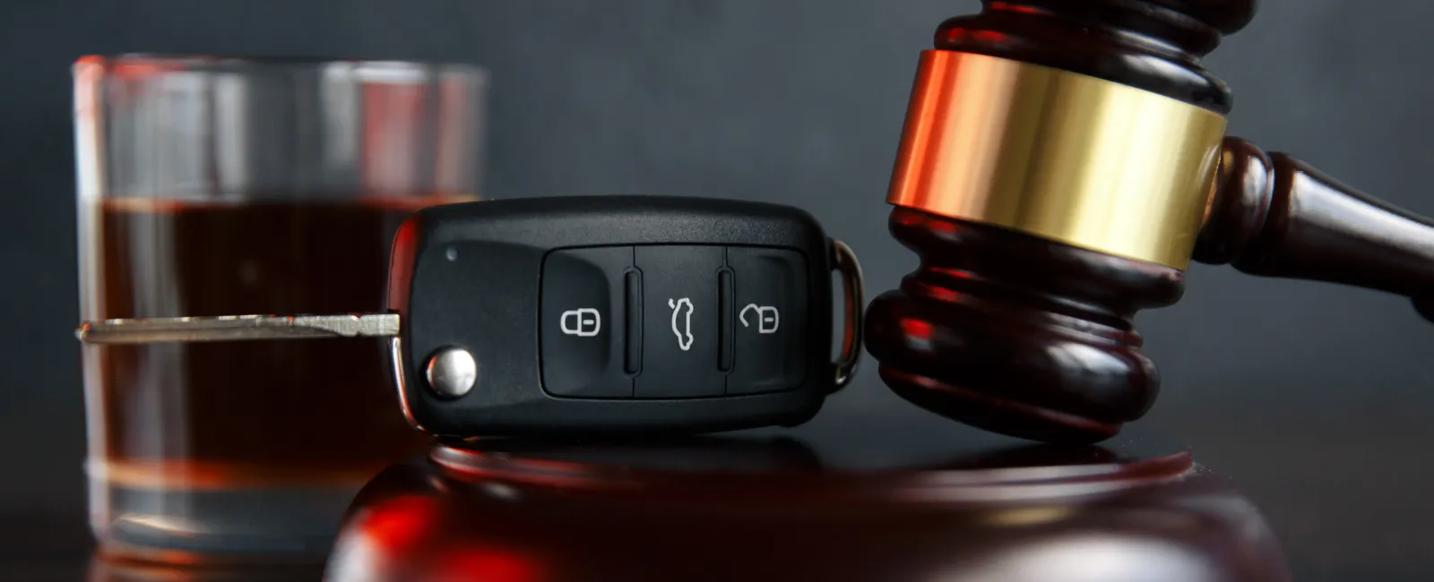 Car key, judge gavel, and a glass of dark liquid representing DUI and legal consequences.