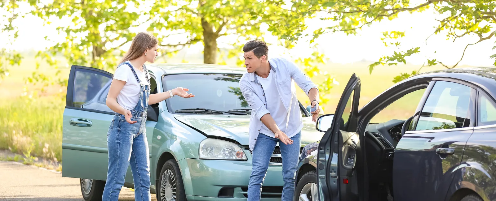 Two people arguing next to their cars after a minor collision on a sunny road with a warning triangle placed on the ground.