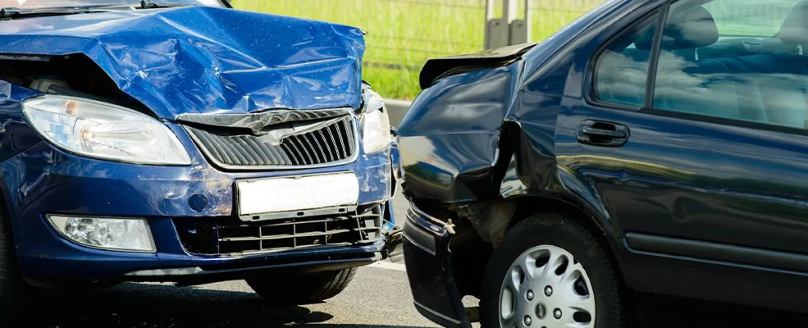 Blue and black cars with severe front-end damage after a collision on a road.