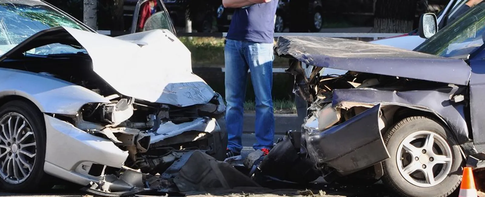 Two cars with severe front-end damage after a collision, person standing nearby assessing the crash scene