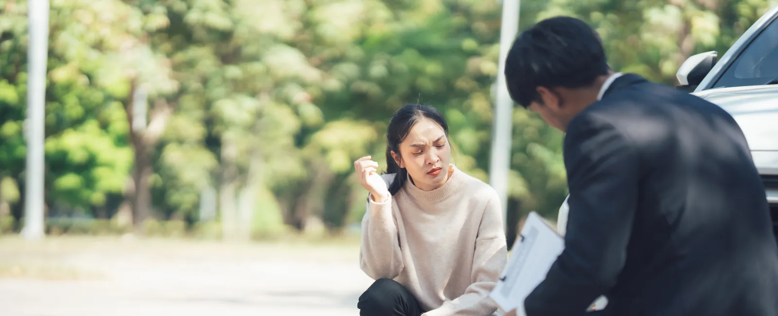 Woman and man crouching by a car examining damage during an insurance claim inspection outdoors