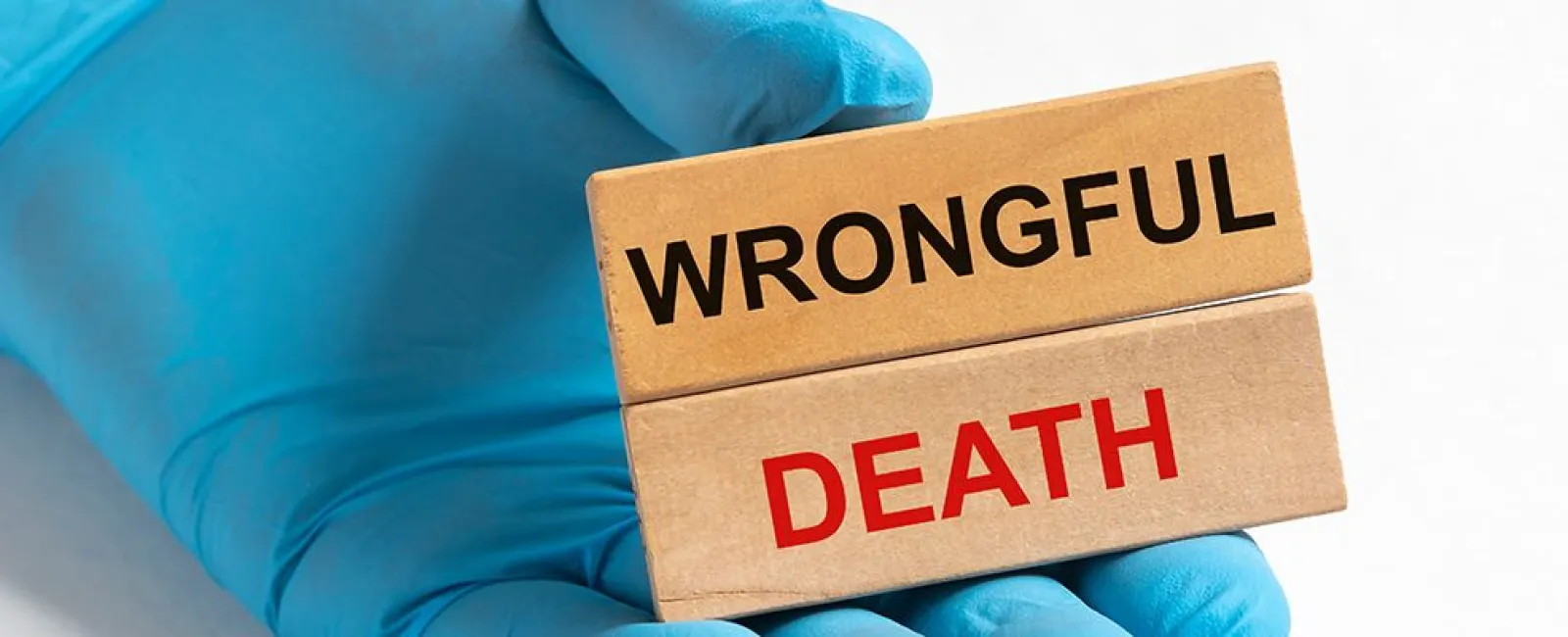 Hand in blue glove holding wooden blocks with the words Wrongful Death against white background