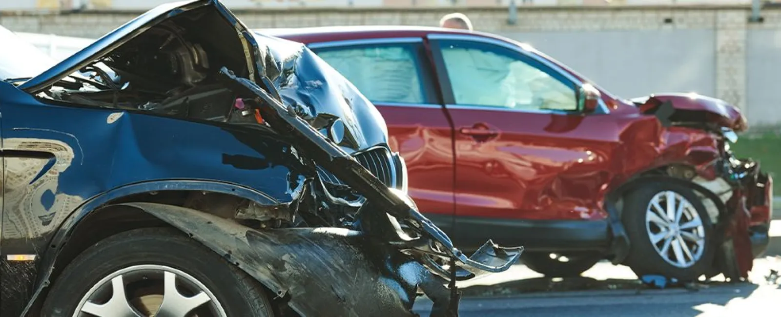Front-end damage on a blue and a red car after a collision in a parking area on a sunny day