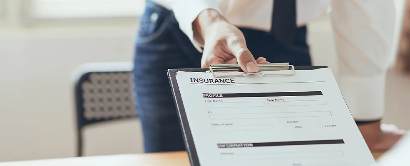 Person holding an insurance application form on a clipboard ready for signing at a desk.