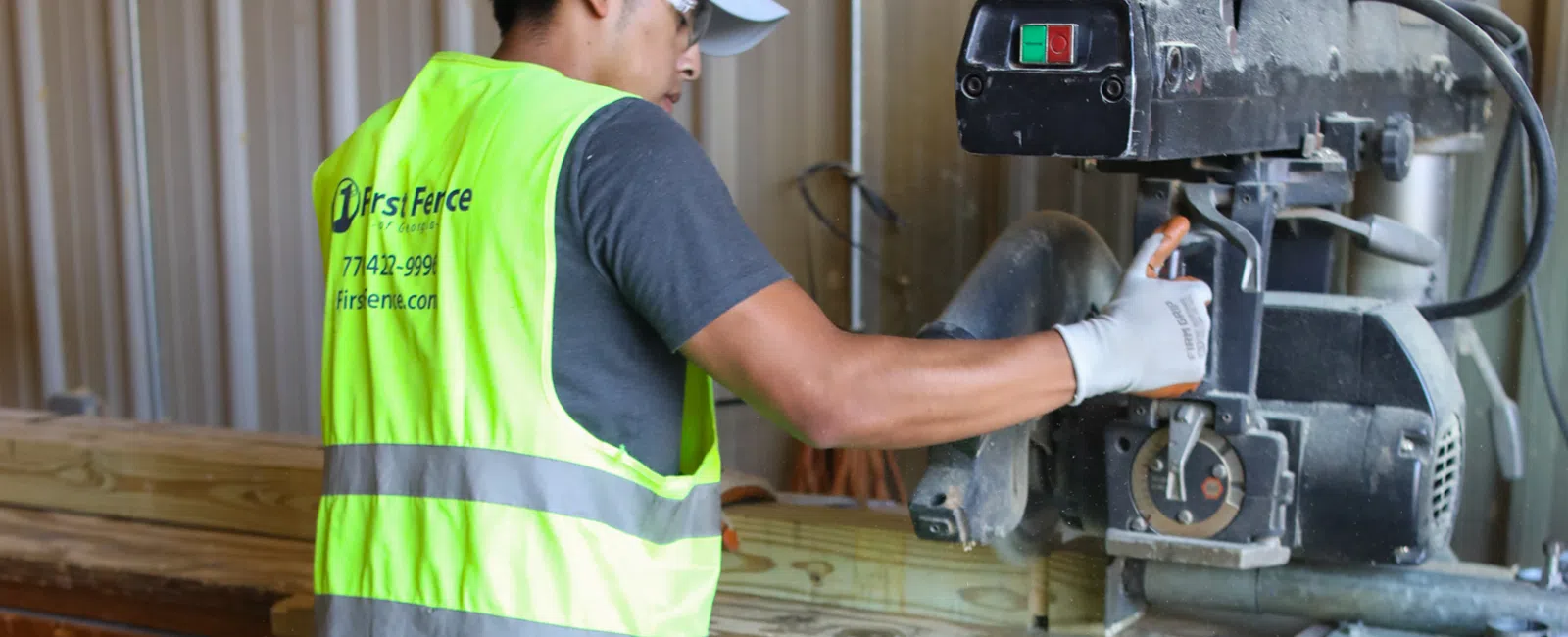 Worker wearing a safety vest using a power saw to cut wood in a workshop