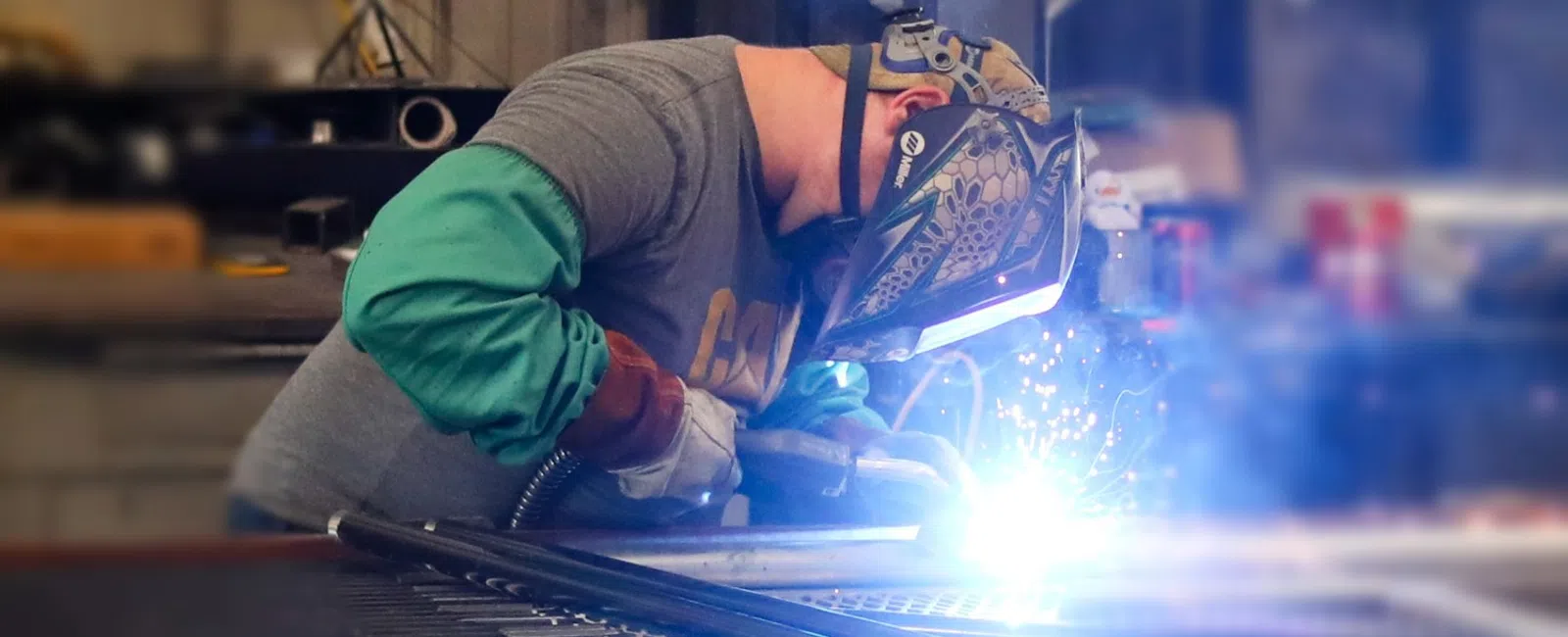 Welder wearing protective gear welding metal pipes producing bright sparks in workshop environment
