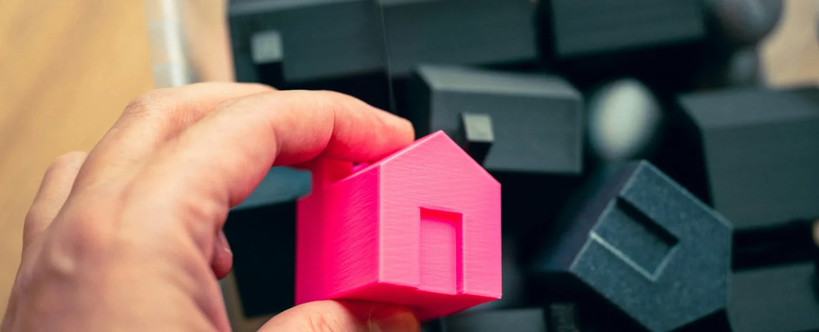 Hand holding a bright pink miniature house among multiple black miniature houses in a container.